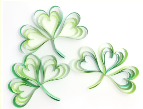 Three shamrocks made of paper strips folded into heart shapes and attached together in a shamrock shape.