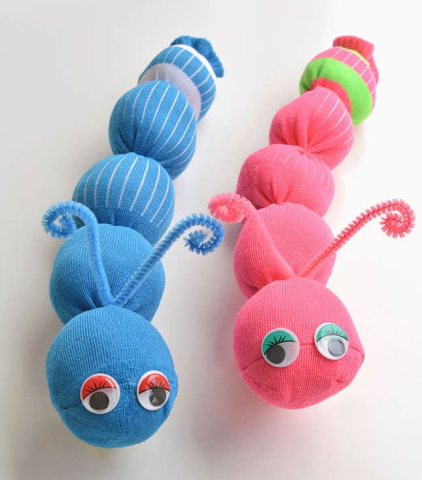Two sock worms made of stuffed socks rubber banded off into sections with pipe cleaner antennae and googly eyes. A blue worm on the left and a pink worm on the right.