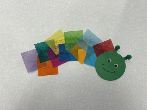 A caterpillar made out of half a paper plate, tissue paper squares, and a construction paper head.