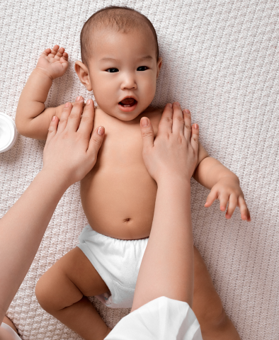 Infant in diaper with caregiver hands giving massage on shoulders and chest area.