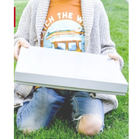Child in an orange shirt holding a plain white flat cardboard pizza box.