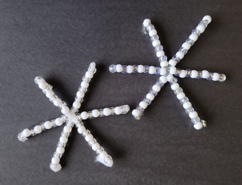 White, clear, and silver glitter beads strung onto white and silver pipe cleaners to make snowflakes shapes.