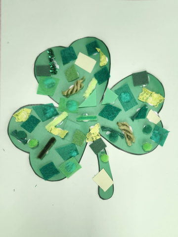 Shamrock with different textures of green craft supplies glued onto it  - lace, yarn, felt, construction paper, pipe cleaners, pom poms.