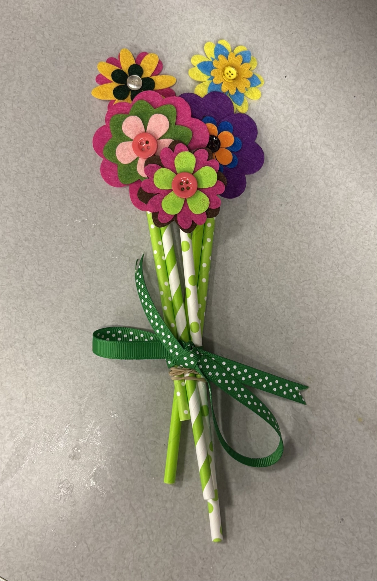 Bouquet of 5 felt flowers with green straw stems and a green ribbon.